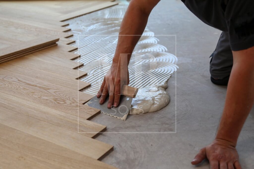 Encollage du support à la spatule crantée pour une pose de parquet collé